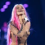 Karol G en concert dans Fortnite pour un événement musical inédit cet été Karol G with a mic in hand, pictured smiling as she is singing.