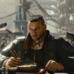 A large, muscly bloke eating noodles at a bar while two people point pistols at him from behind in Cyberpunk 2077.