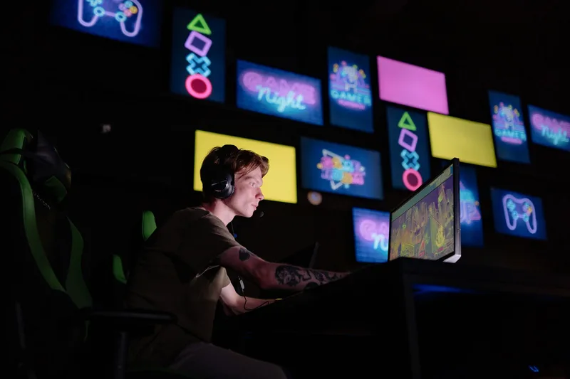 A focused gamer plays e-sports in a neon-lit room, surrounded by digital screens. (stock photo via Pexels)